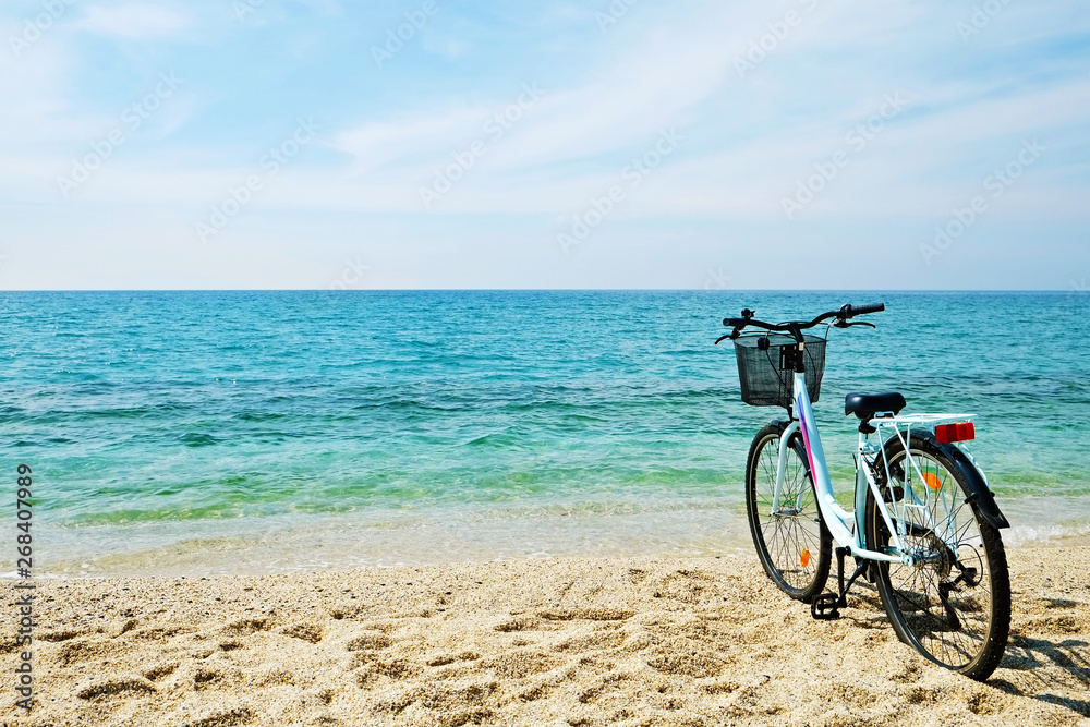 Obraz premium Feminine bicycle of comfort class with empty basket on the sandy beach of mediterranean sea. Blue cruiser bike on sunny day at sea shore with a lot of copy space for text.