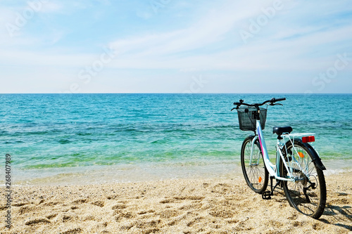 Feminine bicycle of comfort class with empty basket on the sandy beach of mediterranean sea. Blue cruiser bike on sunny day at sea shore with a lot of copy space for text.