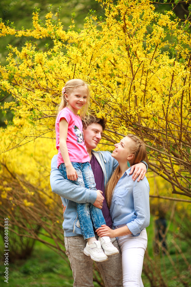 Fototapeta premium Young loving couple of parents with child daughter in park on background of yellow flowering tree