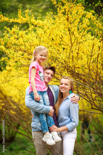 Young loving couple of parents with child daughter in park on background of yellow flowering tree