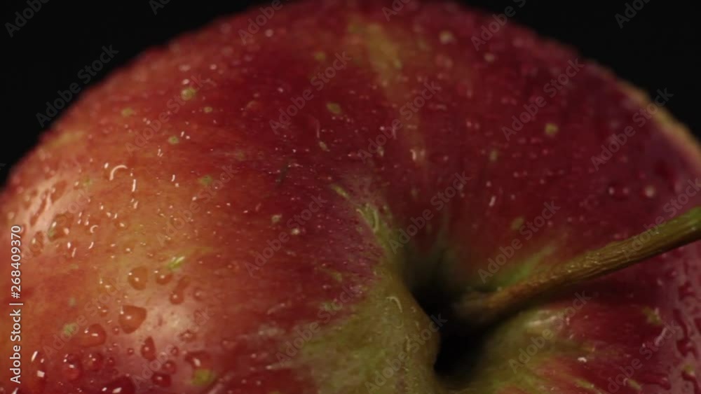 Red apple with water droplets on a black background. Apple skin in extreme macro close up with a rotational camera move.