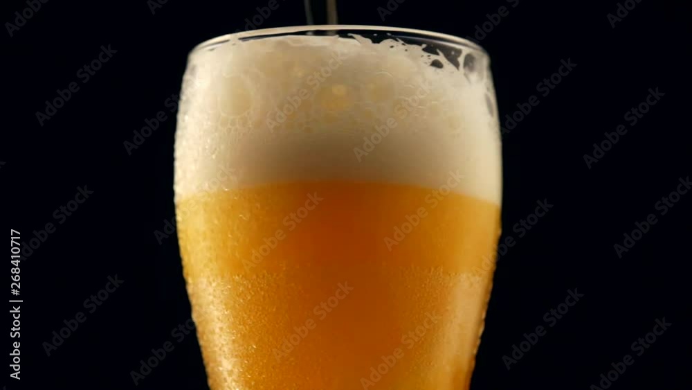 Beer is pouring from the top into the glass. Slow motion. Beer is poured into a glass on a black background. Beer is pouring from the top into the glass. Slow motion. Beer is poured into a glass on a black background.