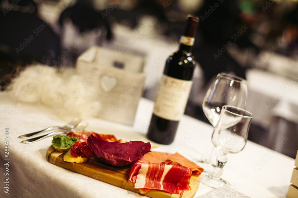 Table setting: white plates, rustic cloth with salami, cheese, vine, ham and wine bottle