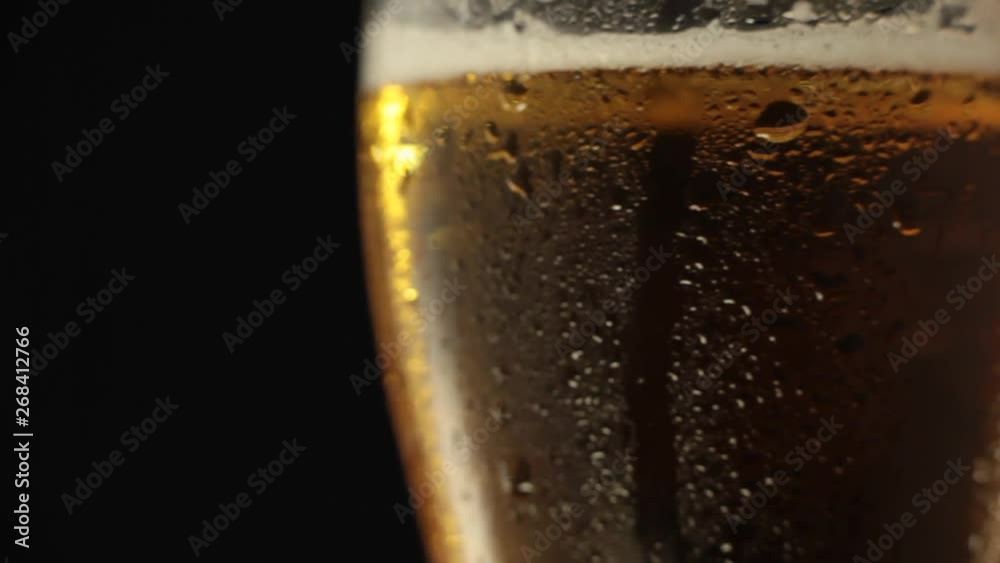 Cold light beer in a glass rotates on a black background. Glass of beer turns slowly around its axis. Cold light beer in a glass rotates on a black background. Glass of beer turns slowly around its axis.