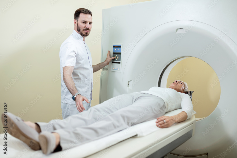 Radiologist preparing a patient for an MR scan examination at clinic.