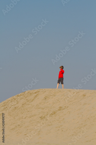 Blond boy in red sweater having fun on sand dunes in Holland