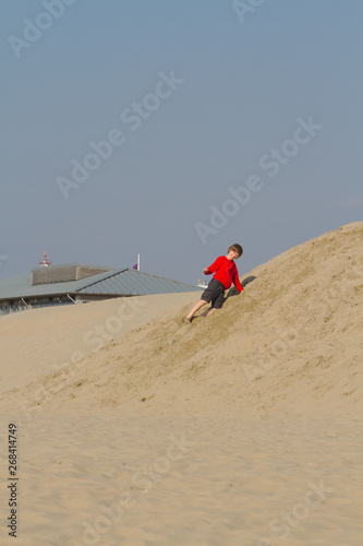 Blond boy in red sweater having fun on sand dunes in Holland