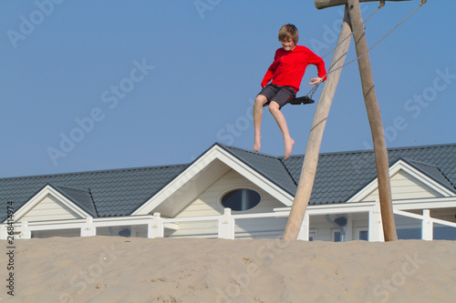 Blond boy in red sweater having fun on sand dunes in Holland