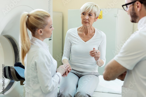 Mature female patient and two radiologists talking after CT scan examination at clinic.