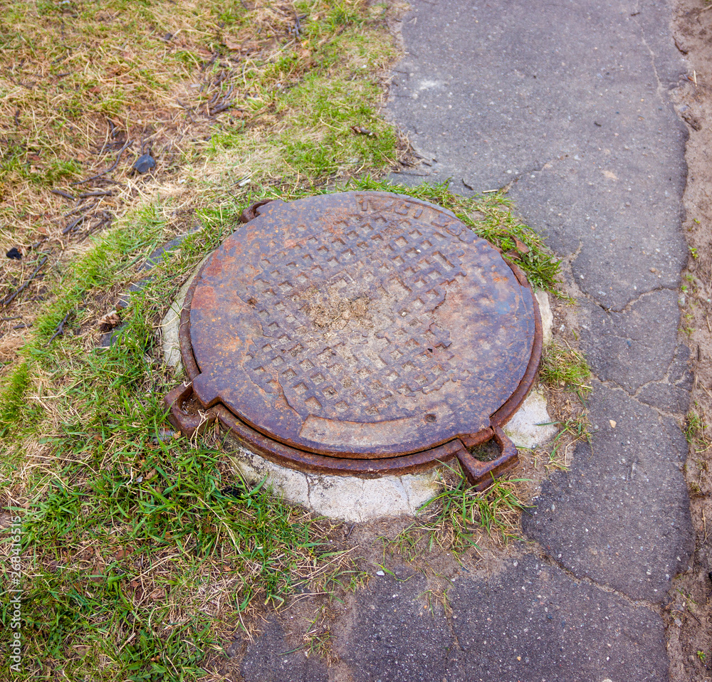 sewer well on the asphalt path next to the lawn