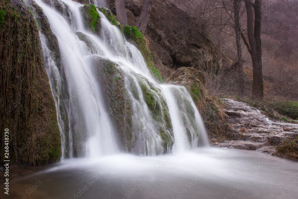 Long exposure view of a sunlit waterfall with soft streams of water falling down red rocks covered by green moss