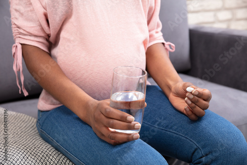 Pregnant Woman Holding Glass Of Water And Vitamin Pill