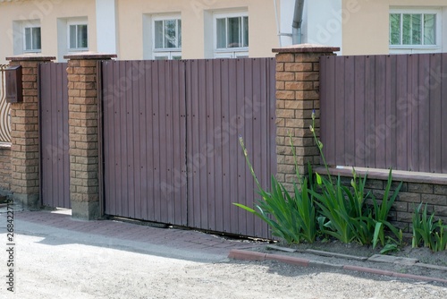 a large brown gate and part of a fence made of metal and bricks outside in green vegetation