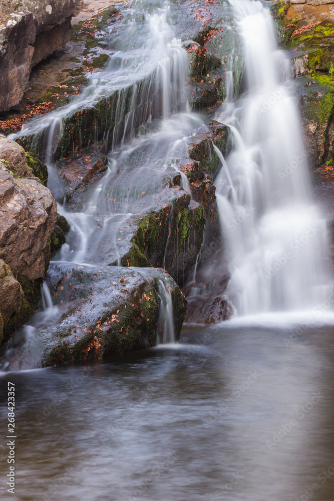 Fototapeta premium Gorgeous mountain creek waterfall cascading down the rocky cliff and colorful autumn red leaves, close-up