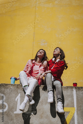 Two happy girls sitting together on parapet