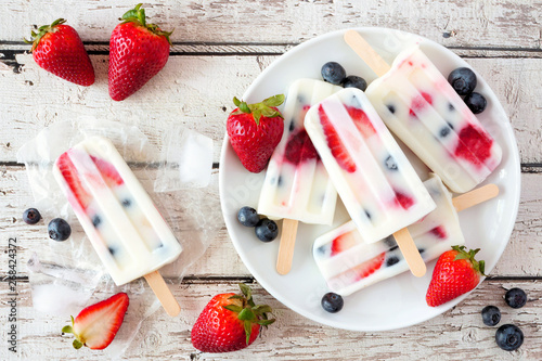 Healthy strawberry blueberry yogurt popsicles on a plate, above view summer table scene against a white wood background photo