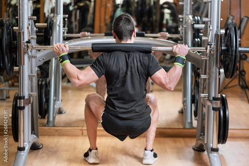 sport, bodybuilding, lifestyle and people concept - young man with barbell doing squats in gym .