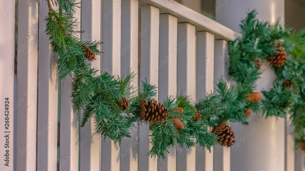 Traditional garland with pine cones draped on the white railing of a building Traditional garland with pine cones draped on the white railing of a building