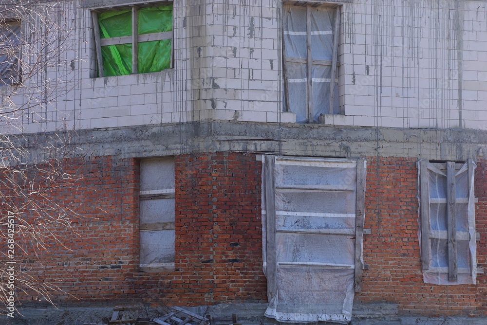 wall of an unfinished house of gray and brown bricks with windows wall of an unfinished house of gray and brown bricks with windows