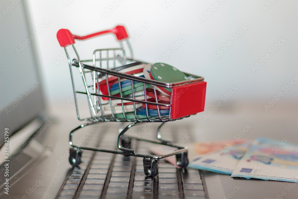 Casino chips in a trolley and euro banknotes on a computer. Online Gambling addiction concept