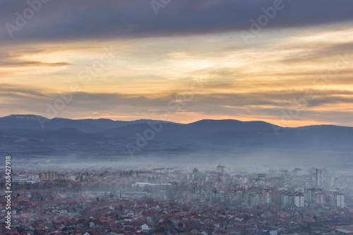 Stunning, soft view of golden sunset sky above scenic cityscape covered by haze and mist