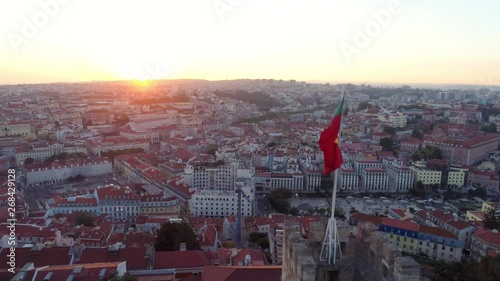 Aerial view medieval fortress on hill top in Lisbon. Drone flying above moorish Castelo de Sao Jorge near flapping poruguese flag on the wall and people enjoying picturesque cityscape at sunset photo