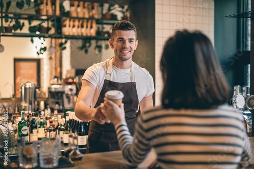 Friendly barista smiling and giving coffee to the client