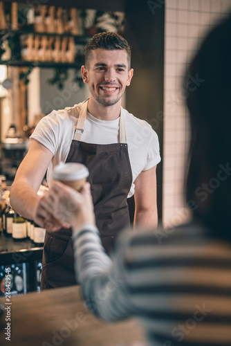 Waist up of friendly barista smiling to the cafe visitor