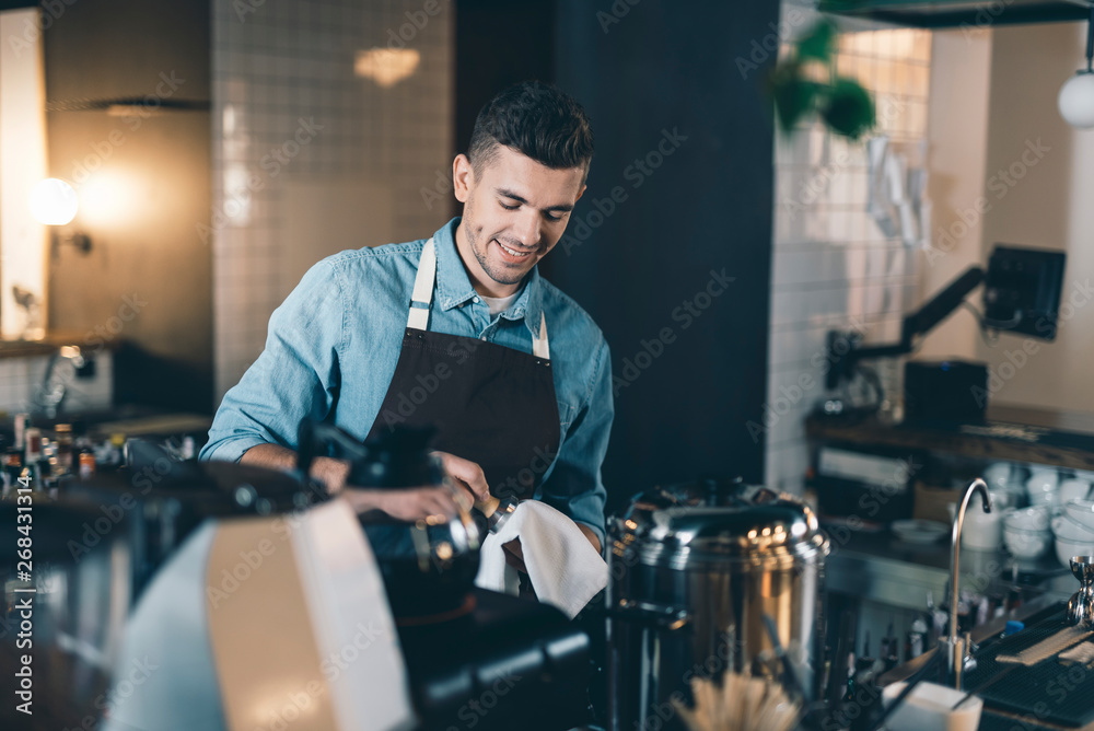 Smiling young man drying clean tamper with soft towel Smiling young man drying clean tamper with soft towel
