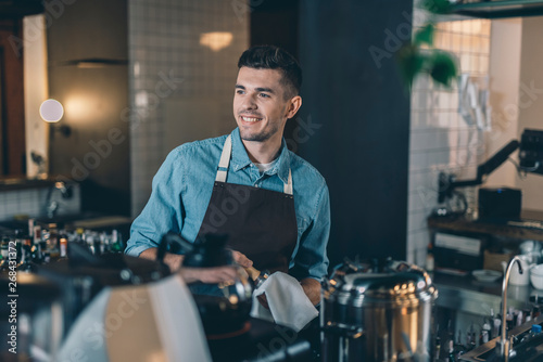 Confident barista looking away while cleaning tamper