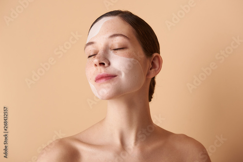 Cute relaxed girl with mask on her face standing against beige background