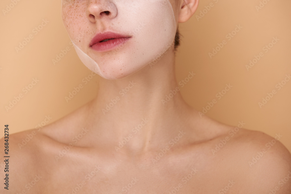 Young woman with white mask on her face standing against beige background