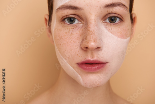 Cute girl with white mask on face posing against beige background