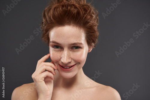 Joyful red-haired girl standing against gray background