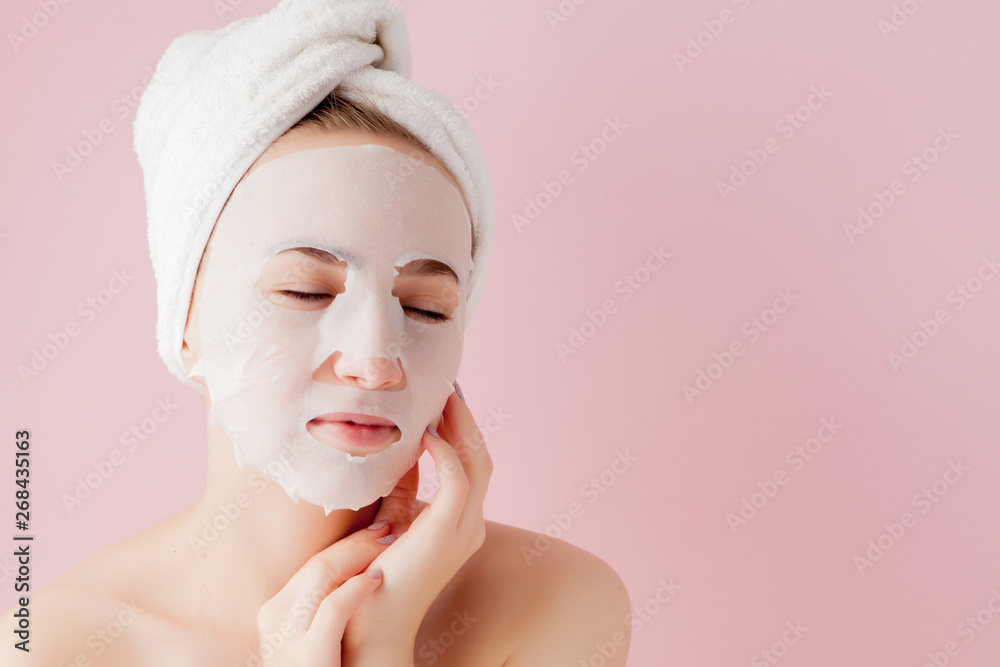 Beautiful young woman is applying a cosmetic tissue mask on a face on a pink background Beautiful young woman is applying a cosmetic tissue mask on a face on a pink background