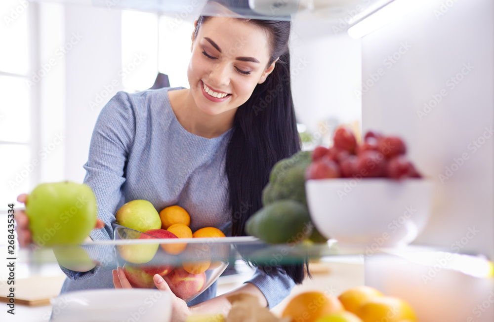 Smiling woman taking a fresh fruit out of the fridge, healthy food concept