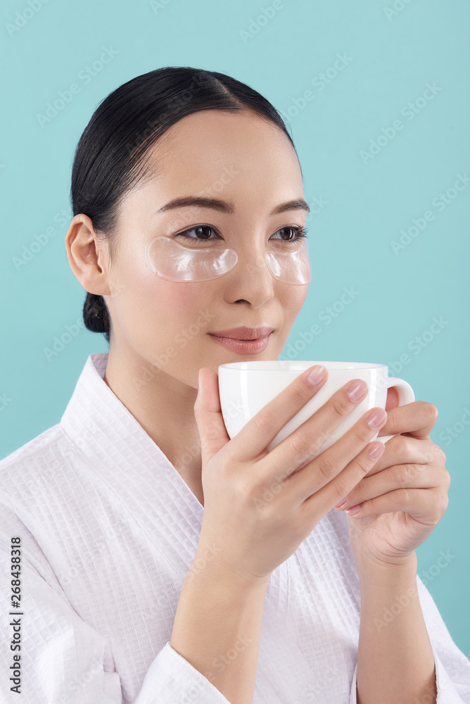 Half length of Asian woman in white bathrobe drinking tea in studio Half length of Asian woman in white bathrobe drinking tea in studio