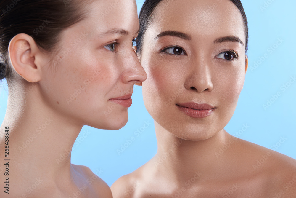Portrait of two naked attractive women situating against blue background Portrait of two naked attractive women situating against blue background