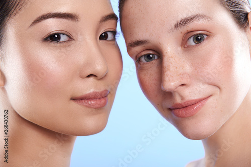 Close up of smiling interracial attractive women situating against blue background