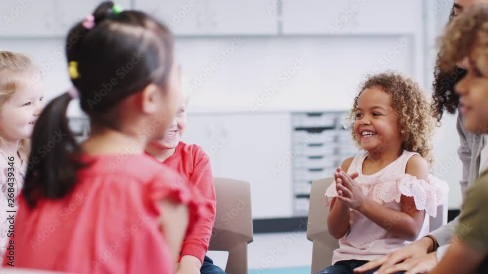 Infant school kids and teacher having a group high five in class after learning, selective focus