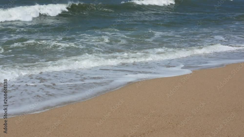 Panning shot of waves breaking on sandy beach as water flows over the sand Panning shot of waves breaking on sandy beach as water flows over the sand