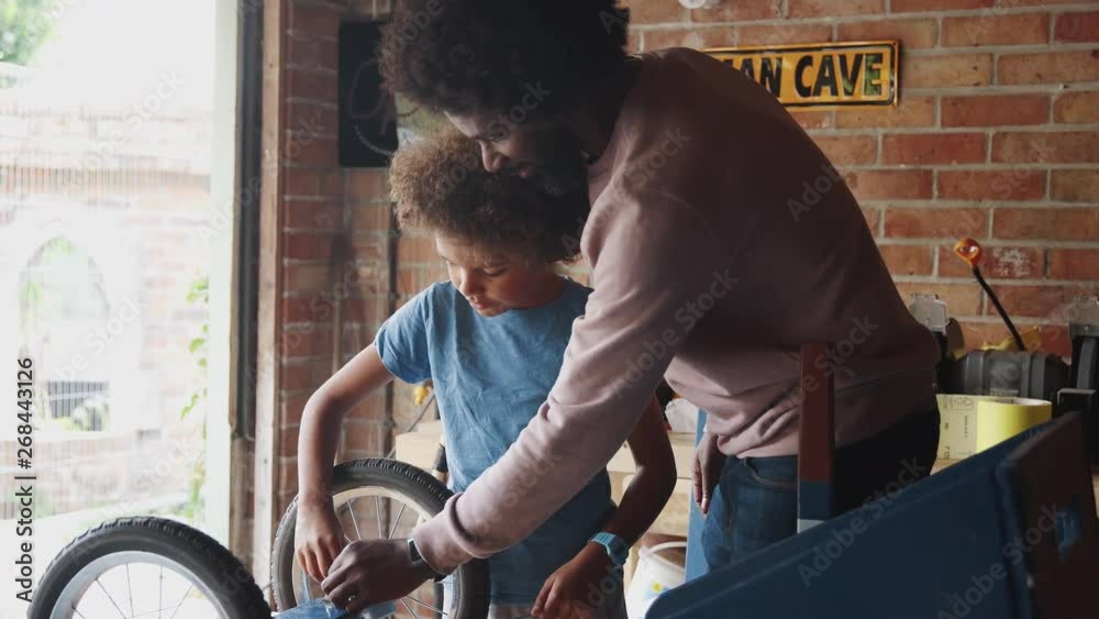Middle aged father helping his pre teen son use a spanner on the wheel of his go kart on a workbench in their garage, selective focus