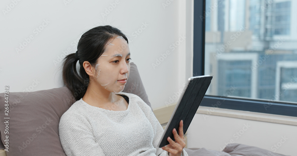Woman use of tablet and apply paper mask on face at home Woman use of tablet and apply paper mask on face at home