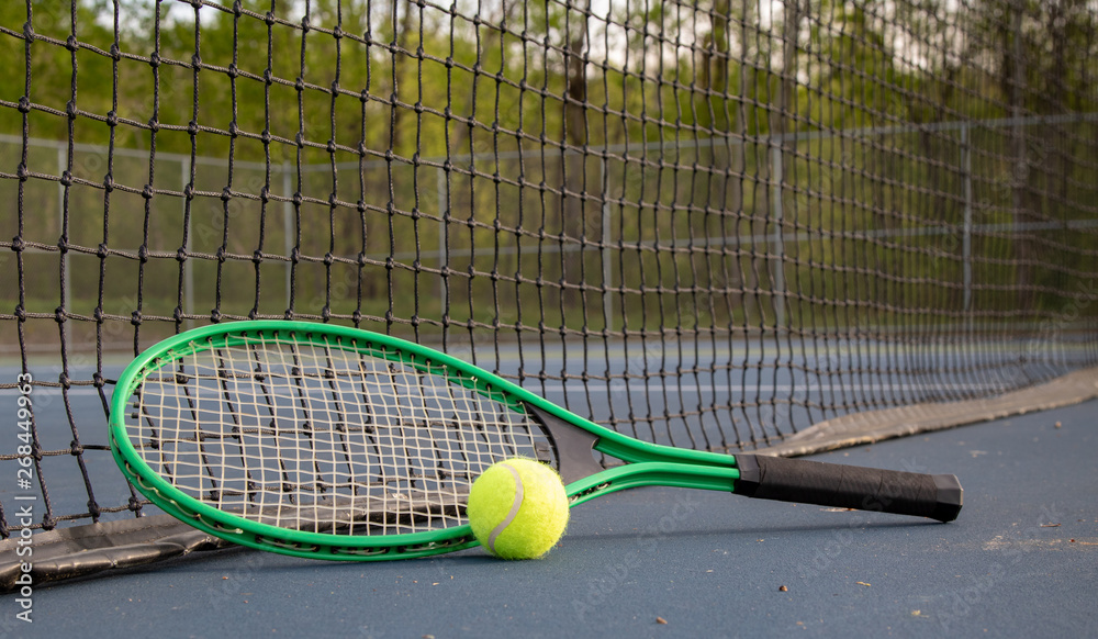 Close up of tennis ball and racket on court with net in the background 