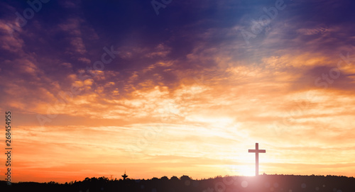 black cross religion symbol silhouette in grass over sunset or sunrise sky