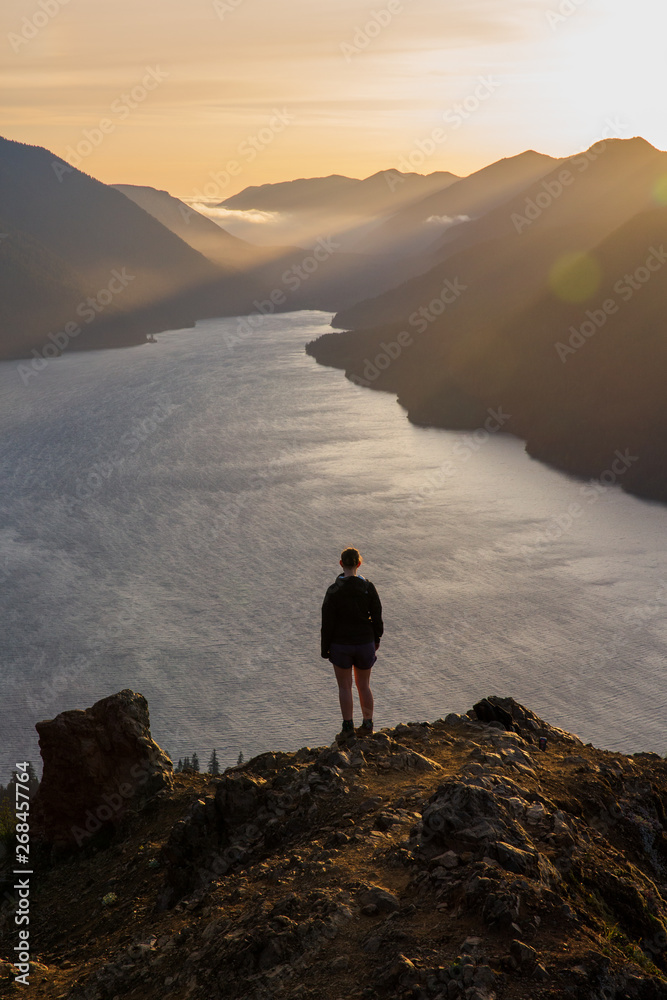 Person on mountain top overlooking lake at sunset with golden light
