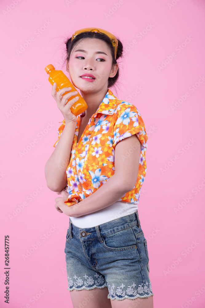 The girl holds a bottle of orange juice on a pink background. The girl holds a bottle of orange juice on a pink background.