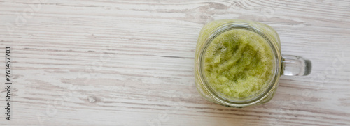 Glass jar mug filled with green celery smoothie on a white wooden background, top view. Overhead, flat lay. Copy space.