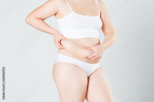 Woman holding fold of skin on thick belly, fat female body on gray background