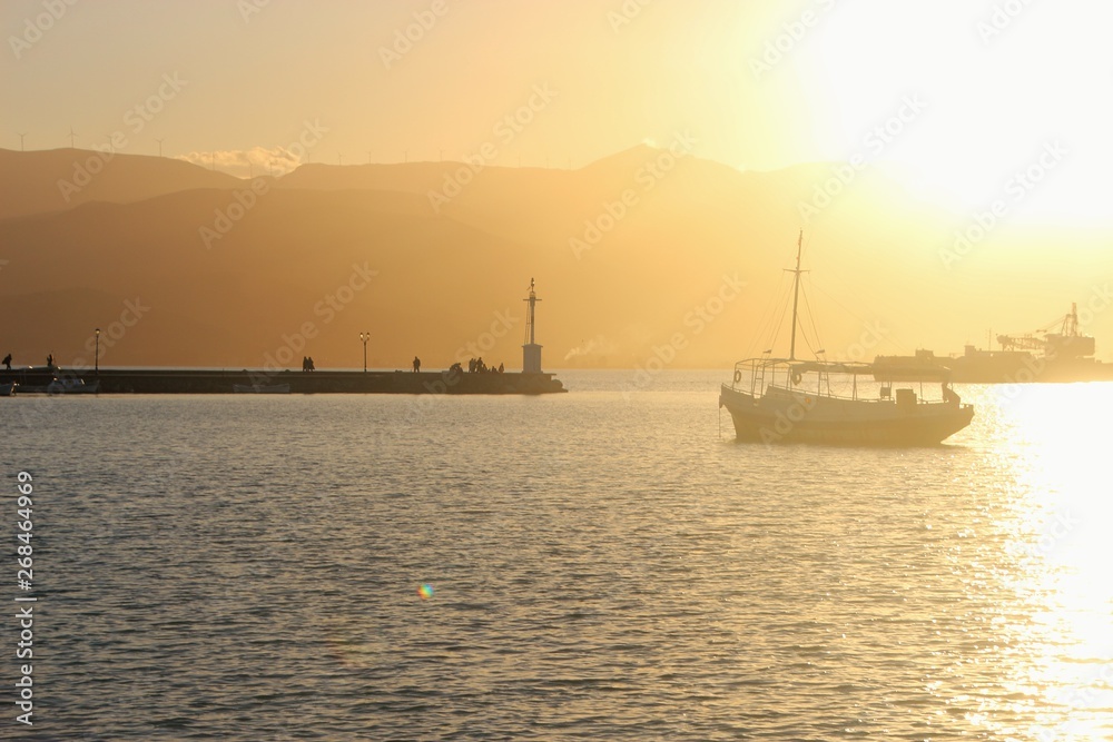 Sunset above the mediterranean sea. In the bay of Nafplio. Peloponnese, Greece.  Mole and lighthouse of Nafplio and boat. South-east Europe.